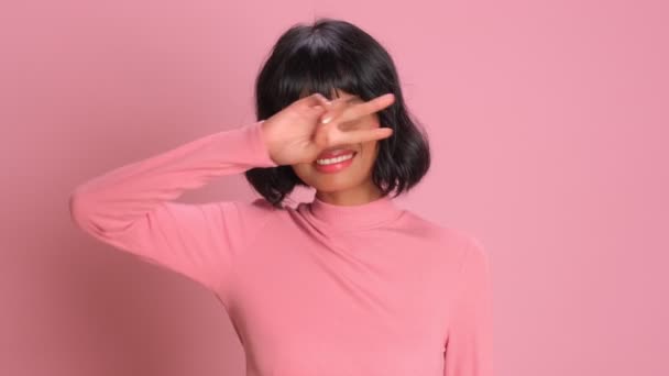 Смішна змішана раса молода жінка робить знак диско і танцює на рожевому фоні — стокове відео