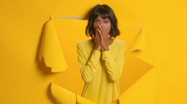Şok olmuş genç bir kadın sarı arka planda büyük bir inanmazlık gösterir.