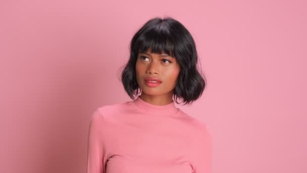 Dark skinned female looks upwards concentrated over pink background — Stock Video