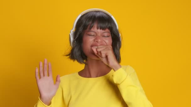 Mujer alegre escucha música agradable en los auriculares y sobre fondo amarillo — Vídeo de stock