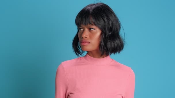 Serious dark skinned female looks away attentively notices over blue background — Stock Video