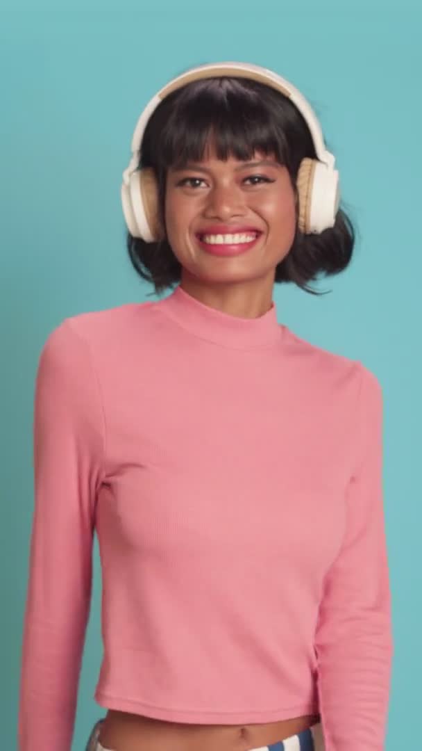 Perempuan muda ras campuran tersenyum secara luas mendengarkan musik di headphone di atas dinding biru — Stok Video