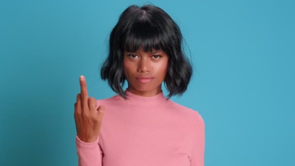 Huysuz Afro-Amerikalı kadın mavi arka planda poker suratlı orta parmaklarını gösteriyor.. — Stok video