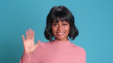 Woman waves her hand and greets smiling broadly at the camera, meeting new people.