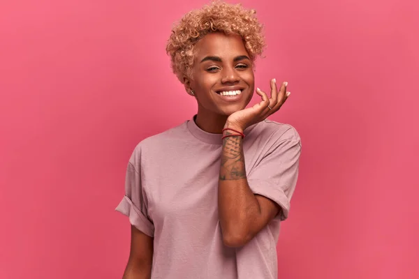 Mujer afro-americana positiva sonriendo sinceramente sobre fondo rosa. — Foto de Stock