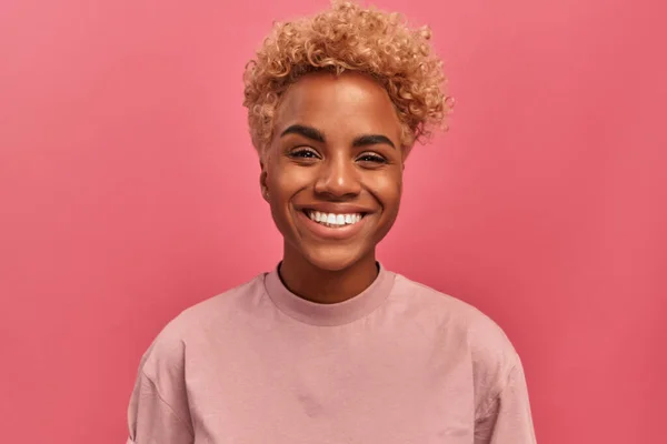 Estúdio retrato de uma mulher de pele escura de bom humor em pé sobre um fundo rosa. — Fotografia de Stock