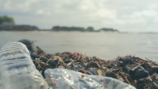 Plastflaskor, påsar och annat skräp som dumpats på mörk sand i havsstranden — Stockvideo