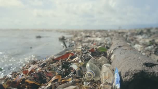 Garrafas de plástico, sacos e outros resíduos despejados na areia escura da praia oceânica — Vídeo de Stock
