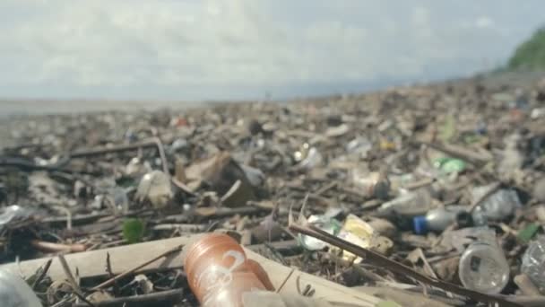 Plastikowe butelki, torby i inne śmieci wyrzucane na ciemny piasek plaży oceanicznej — Wideo stockowe