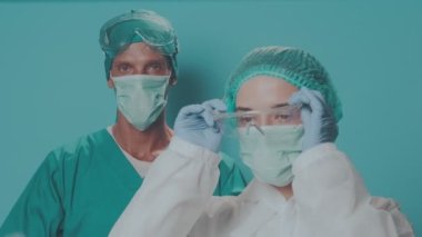 Koruyucu Maskeli ve Biyolojik Tehlike Koruyucu Kıyafetli iki doktor kameraya bakıyor.