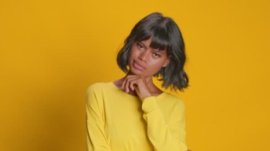 Düşünceli ifadeli ciddi bir kadın sarı arka planda karar verir.