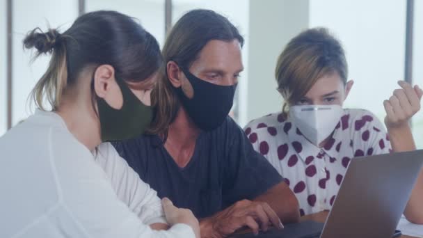 Команда колег з маскою для обличчя обговорює онлайн-проект, використовуючи ноутбук на робочому місці — стокове відео