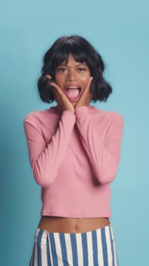 Şok olmuş gibi bakan bir kadın mavi duvarın üzerinde şaşırtıcı hareketler yapar.