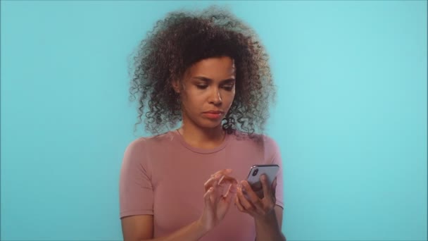 Młoda afrykańska kobieta patrząc na telefon widząc złe wieści na różowym tle — Wideo stockowe