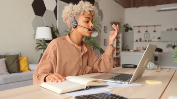 Afro businesswoman wear headset talk by conference call via laptop at home office — Stock video