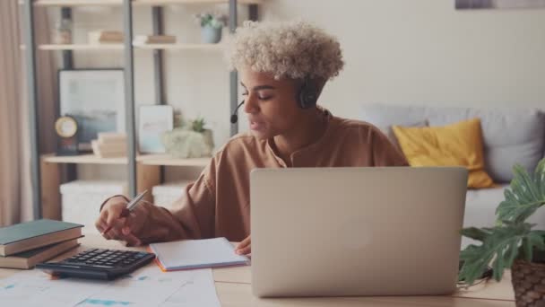 Afro kobieta nosi słuchawki rozmowy z klientem obliczyć rachunki online na laptopie — Wideo stockowe