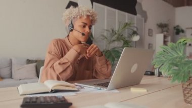 Kulaklık takan Afrikalı bir kız öğrenci dizüstü bilgisayara bakıyor ve internetten Webinar izliyor.