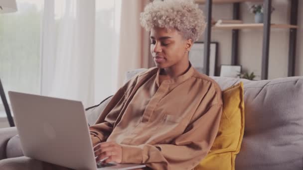 Gericht Afrikaanse vrouw typen op laptop surfen op internet met behulp van apps zitten op de bank — Stockvideo