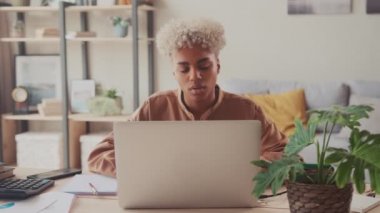 Düşünceli Afro kadın dizüstü bilgisayarda çalışıyor. Pencere mesafesine bakıyor ve plan yapıyor.