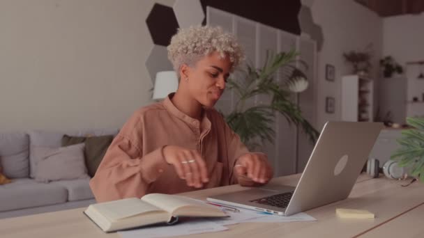 Sonriente joven mujer africana mirando a la computadora portátil y libro de aprendizaje en casa — Vídeos de Stock