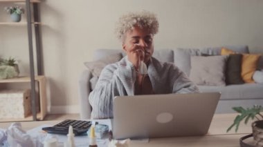 Ekoseli, genç, hasta Afrikalı bir kadın laptopta ilaçlarla çalışıyor.