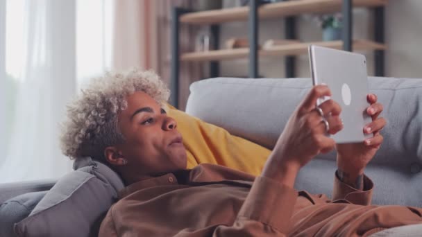 Femme africaine couchée sur le canapé étudiant des applications de conception sur tablette numérique — Video