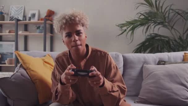 African woman with blonde hair playing video game using gamepad on sofa home — Stock Video