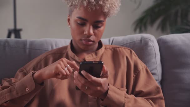 Mujer africana descansando en el sofá con el teléfono inteligente disfrutar de un dispositivo inalámbrico moderno — Vídeo de stock