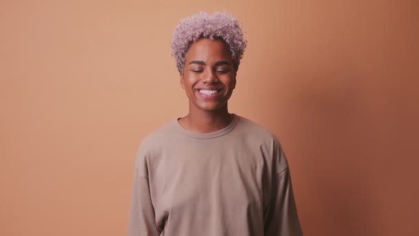 Junge Afrikanerin lächelt fröhlich und zeigt ihre weißen Zähne über beige Wand — Stockvideo
