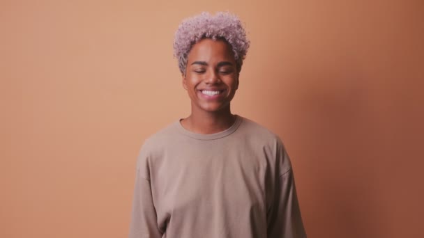 Young African woman smiling cheerfully showing her white teeth over beige wall — ストック動画