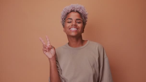 Оптимістична щаслива темношкіра жінка з позитивним виразом обличчя, показує знак V — стокове відео