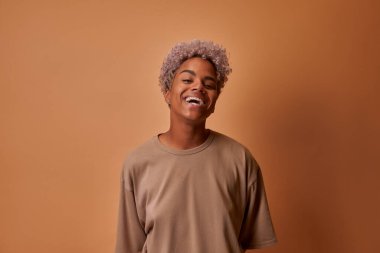 Genç Afrikalı kadın bej duvarın üzerinde beyaz dişlerini göstererek gülümsüyor.