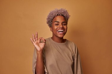 Siyah saçlı, pozitif tenli bir kadının portresi, iyi bir jest yapıyor.