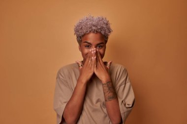 Şaşırmış esmer tenli kadın neşeli görünüyor, ağzını ellerle kapatıyor..