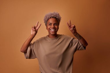 İyimser sevinçli koyu tenli, yüzünde pozitif bir ifade olan kadın, V işareti gösteriyor.