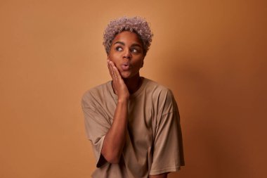 Kıvırcık saçlı, koyu tenli bir kadın kahverengi arka planda el ele tutuşuyor.