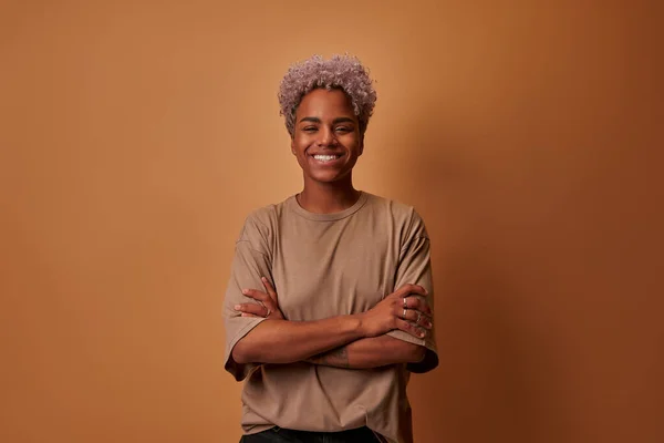 Sorrindo milenar mulher africana de pé com braços dobrados sobre fundo bege — Fotografia de Stock