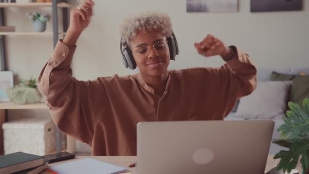 Африканская женщина слушает музыку на рабочем месте, танцуя в наушниках в офисе — стоковое видео