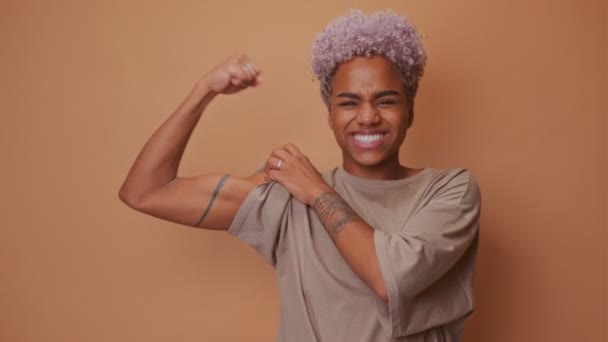 Positiva mujer joven africana plantea brazo muscular muestra bíceps tiene aspecto potente — Vídeos de Stock