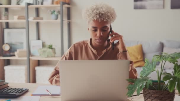 Африканская женщина с ноутбуком разговаривает на смартфоне — стоковое видео