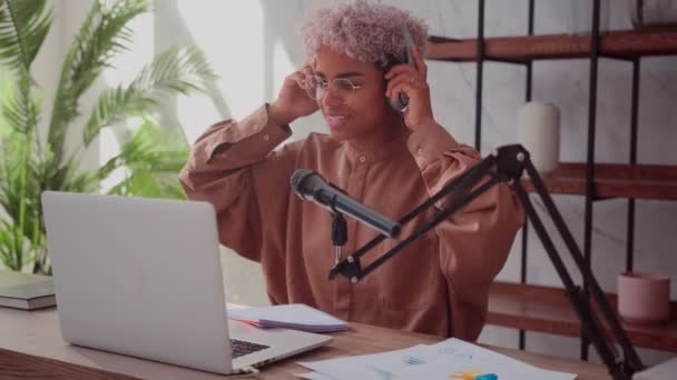 Mulher africana sorrindo usando fones de ouvido sem fio se preparando para gravar podcast — Vídeo de Stock