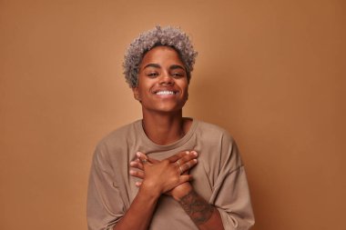 Güzel, heyecanlı, sarışın, esmer tenli kadın ellerini mutlulukla göğsüne koyuyor.