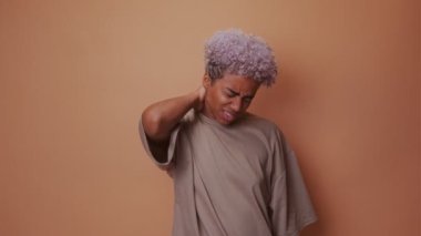 Afrikalı kadın, kas gerilimini ortaya çıkarmak için boynuna masaj yaptığı için yüzünü buruşturuyor.