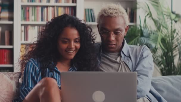 Gelukkig gemengd ras jong paar met behulp van laptop kijken naar het scherm samen op de bank — Stockvideo