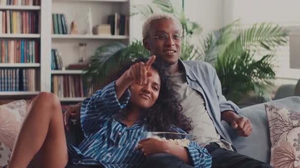 Diverso casal assistindo filme de aventura na TV e comer pipoca sentado no sofá — Vídeo de Stock