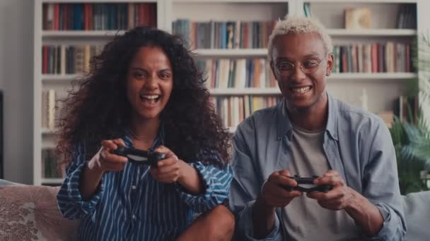 Щаслива змішана гонка пара сидить на дивані Граючи відеоігри за допомогою контролерів — стокове відео