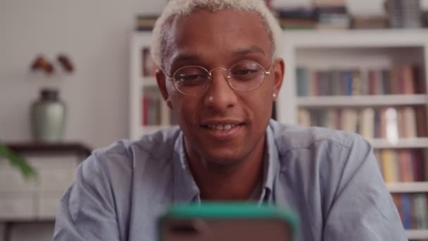 Alegre homem de pele escura com cabelo loiro em casa escritório, usando telefone inteligente — Vídeo de Stock