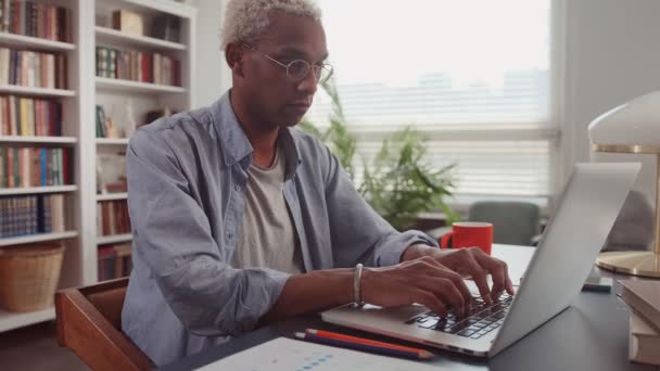 Joven escritor afroamericano escribiendo en el portátil, escribiendo artículo en casa — Vídeos de Stock