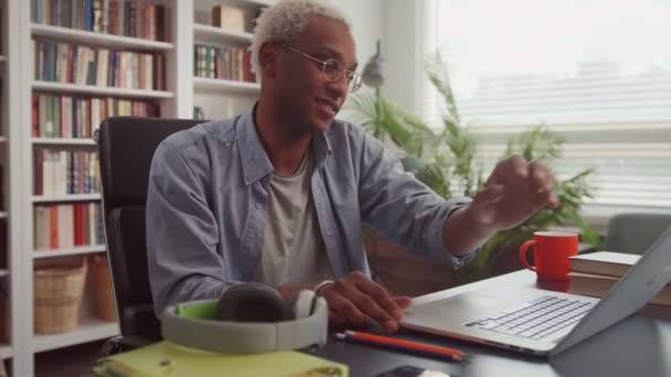 Africain homme ouverture ordinateur portable, port d'écouteurs sans fil et de commencer sa journée de travail — Video