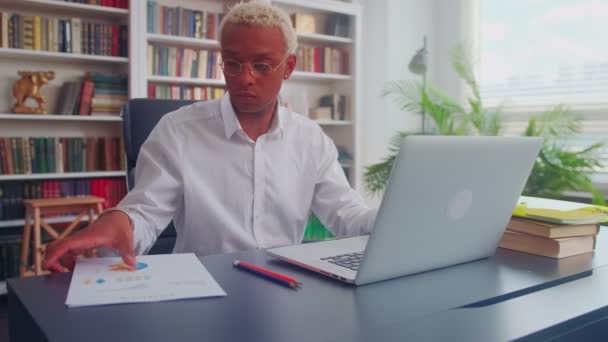 Enfocado hombre africano serio contable celebración de documentos mirando a la computadora portátil — Vídeos de Stock